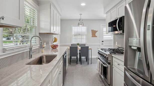 A modern kitchen with white cabinetry, stainless steel appliances, and a dining area with a table and chairs. - MSP/Mall of America/Pond View with garden oasis (Richfield)