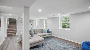 A spacious living room with a grey sectional sofa, a blue bean bag, a grey shag rug, and a large window with a view of greenery.