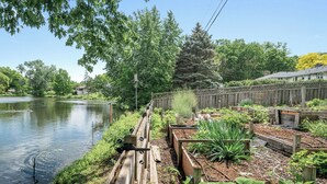 A garden with raised beds and a wooden fence by a lake. - MSP/Mall of America/Pond View with garden oasis (Richfield)