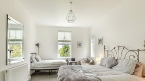 A bedroom with two beds, a desk, a chair, a radiator, and a window with blinds. - Discover a spacious holiday home in Paignton, Devon, accommodating ten guests. (Paignton)