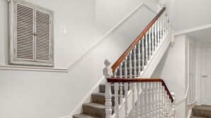 A staircase with white balusters and a wooden handrail, carpeted steps, and a white wall with a window with shutters. - Discover a spacious holiday home in Paignton, Devon, accommodating ten guests. (Paignton)