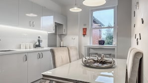 A modern kitchen with white cabinets, a dining table with a glass top, and pendant lighting. - Discover a spacious holiday home in Paignton, Devon, accommodating ten guests. (Paignton)