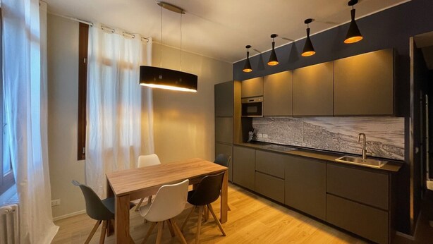 Uma cozinha moderna com mesa e cadeiras de madeira, forno embutido e luminárias pendentes.