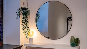 A modern room with a round mirror, a white chair, a small shelf with cacti, and a hanging plant with a lamp. - Stunning Modern City Centre Apartment Retreat (Nottingham)