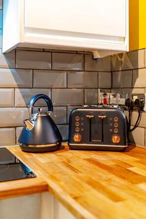 Une cuisine avec une bouilloire noire et un grille-pain noir posés sur un plan de travail en bois.