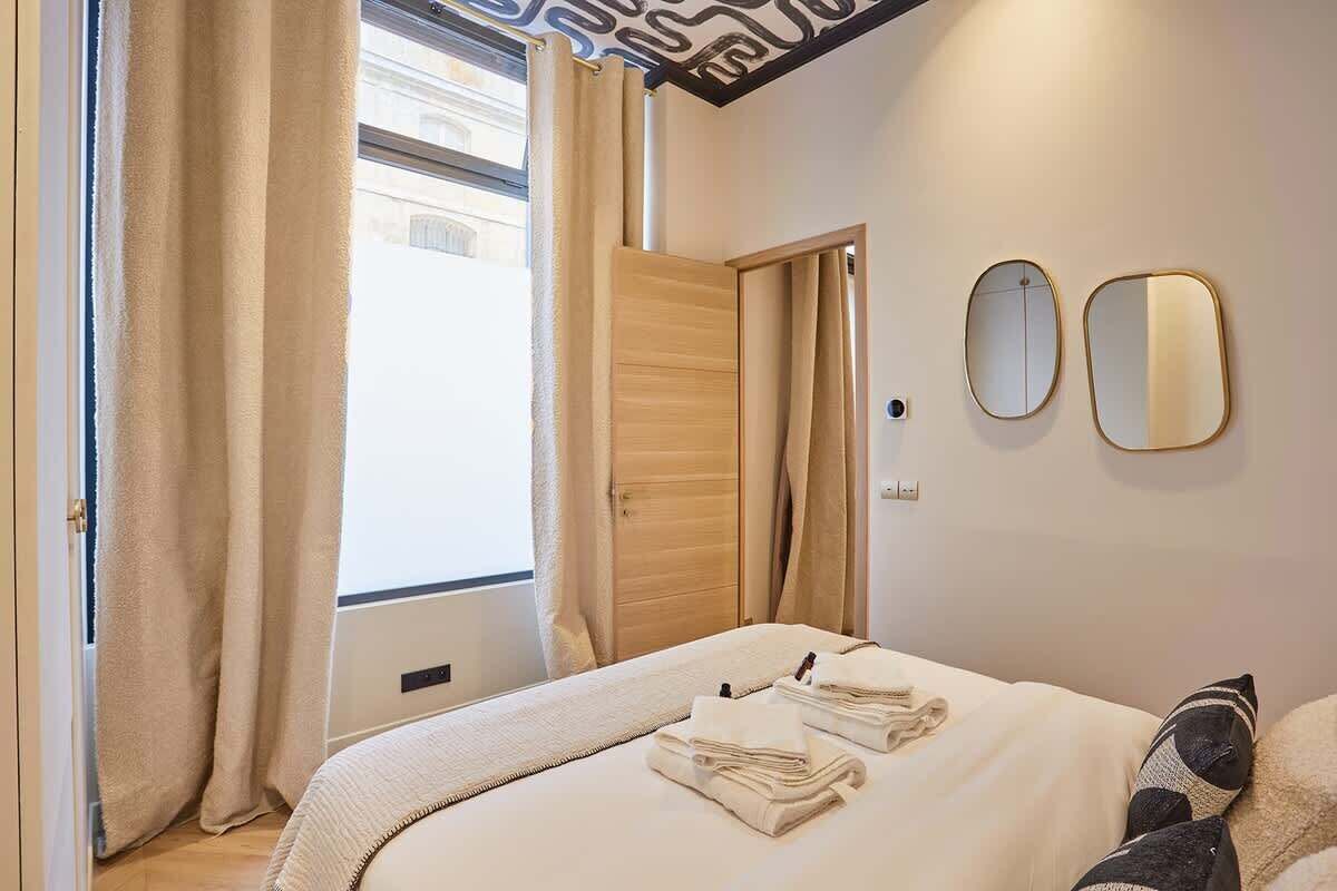 Une chambre d’hôtel avec un lit, une armoire en bois, une fenêtre avec des rideaux et deux miroirs fixés au mur.