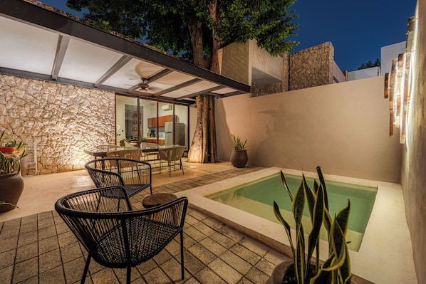 A patio with chairs, a table, a pool, and a stone wall. - Casa Balada Santa Lucia, with Parking by Cercana (Mérida)