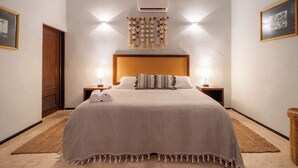 A neatly arranged bedroom with a bed, two bedside tables, a wall-mounted air conditioner, and a hanging light fixture. - Casa Balada Santa Lucia, with Parking by Cercana (Mérida)