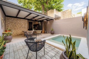 Un espace piscine agrémenté de chaises et d’une table, entouré de murs en pierre et de plantes en pot.