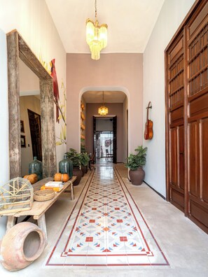 A hallway with a patterned floor, a wooden door, a hanging guitar, and a mirror with wall art. - Casa Balada Santa Lucia, with Parking by Cercana (Mérida)