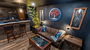 Un espace bar accueillant, avec des tabourets, un comptoir en bois et un coin salon comprenant un canapé en cuir et une table basse.