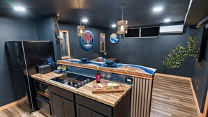 Une cuisine moderne dotée d’un îlot central, de meubles de rangement noirs et d’un plan de travail en bois.