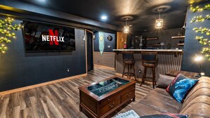 Un salon confortable avec un téléviseur Netflix, un plancher en bois, une table basse et un coin bar.