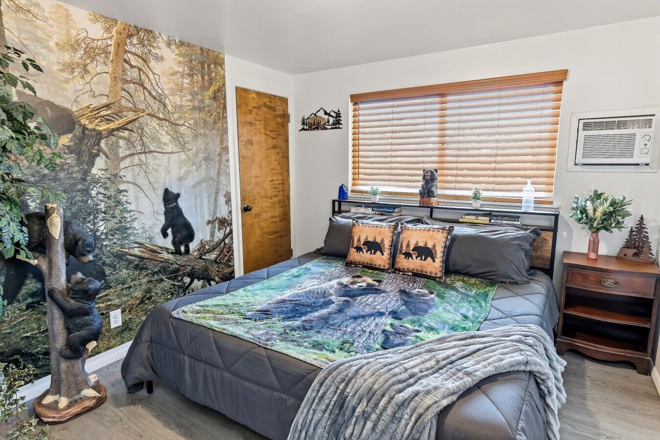 Une chambre avec un grand lit, une fenêtre avec des stores, une table de chevet et une fresque murale.