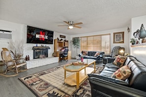 A living room with a fireplace, a black leather sofa, a coffee table, and a TV mounted on the wall.