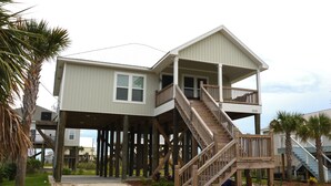 Ein zweistöckiges Strandhaus mit einer Holztreppe, die zu einem Balkon führt.