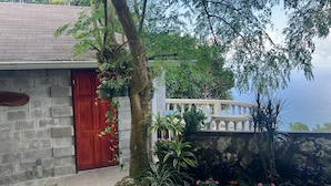 A stone building with a red door, a balcony with a railing, and a view of the sea.