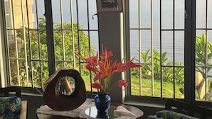 A room with a view of a body of water, a table with a vase of flowers, and two chairs with tropical prints.