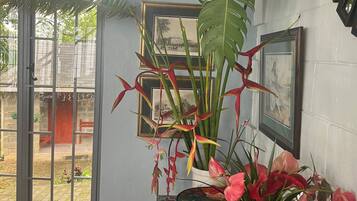Una stanza con un'ampia finestra, una sveglia a muro e un tavolo con un vaso di fiori e banane.