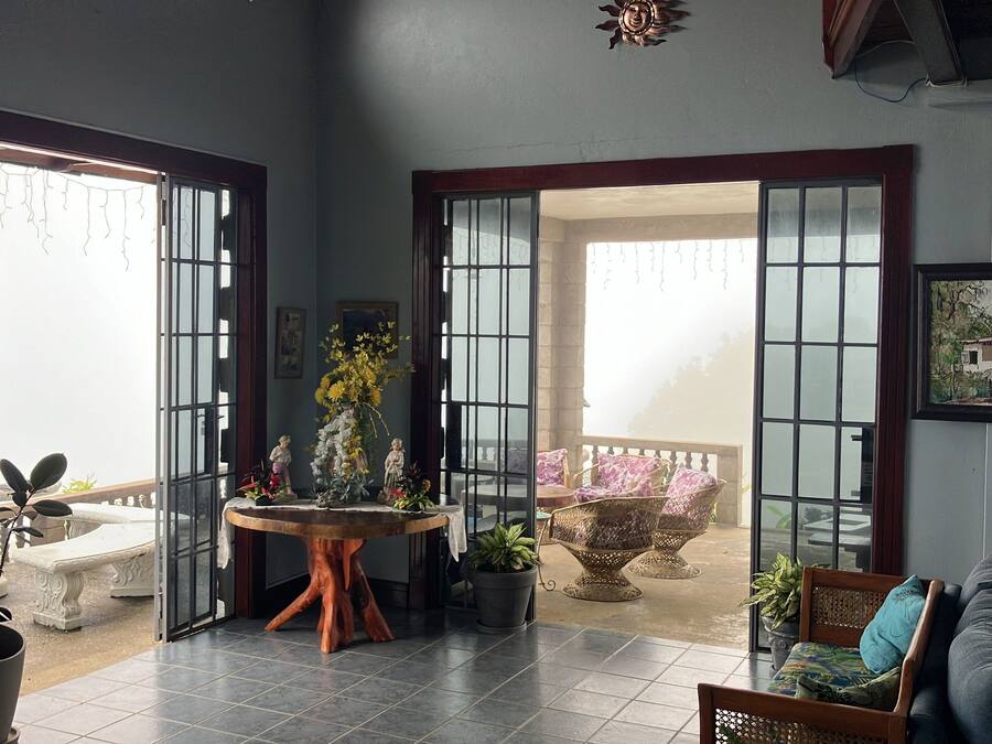 A spacious room with a large open door leading to an outdoor area, a wooden table with plants, and a sofa.