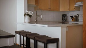 Eine Küche mit Holzausstattung, einer weißen Arbeitsplatte, einem Edelstahlarmaturen und einer Kaffeemaschine, sowie einer Vase mit Blumen.