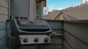 Ein Weber Spirit II Grill mit zwei Drehknöpfen und einer Bedienblende, auf einem Balkon mit Bergblick.