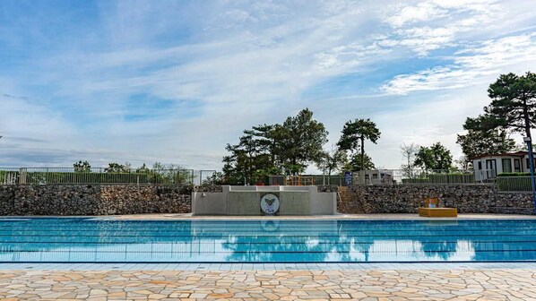 Una piscina con baldosas de piedra, un muro de piedra y árboles al fondo.