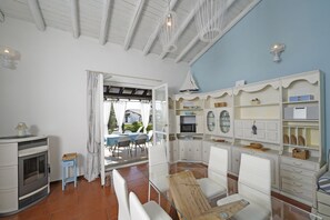 Een kamer met een open haard, witte meubels, een eethoek met stoelen en een tafel, en een keuken met kasten en een magnetron.