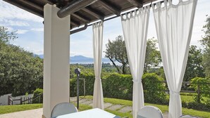 Una terrazza esterna con un tavolo apparecchiato per mangiare, circondata da sedie e coperta da un tendaggio bianco.