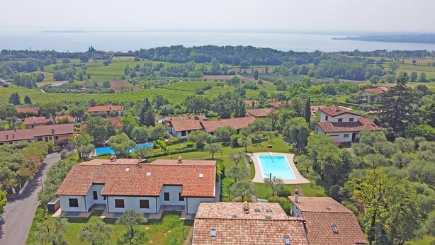 Un quartiere residenziale con case dotate di tetti in tegole rosse, una piscina e vegetazione rigogliosa.