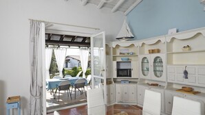 Una stanza con zona pranzo, arredi bianchi, un tavolo in vetro e vista sull'esterno.