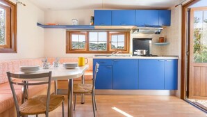 Una cocina compacta con armarios azules, un comedor con una mesa blanca y sillas de mimbre, y vistas a través del ventanal.