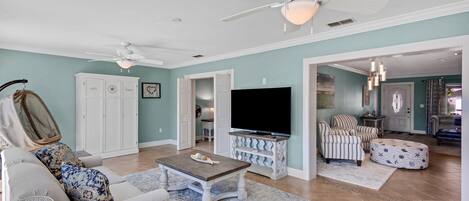 A spacious living room with a ceiling fan, a flat-screen TV, and a comfortable seating area.