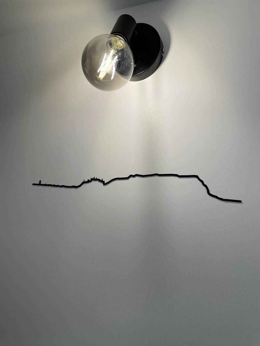 Eine Wand mit einer schwarzen Linienzeichnung und einer Wandleuchte.