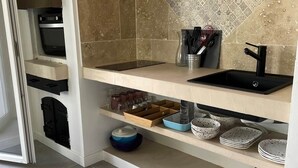 A kitchen with a built-in oven, a sink, and shelves with dishes and utensils. - 3.juju (CASSIS)