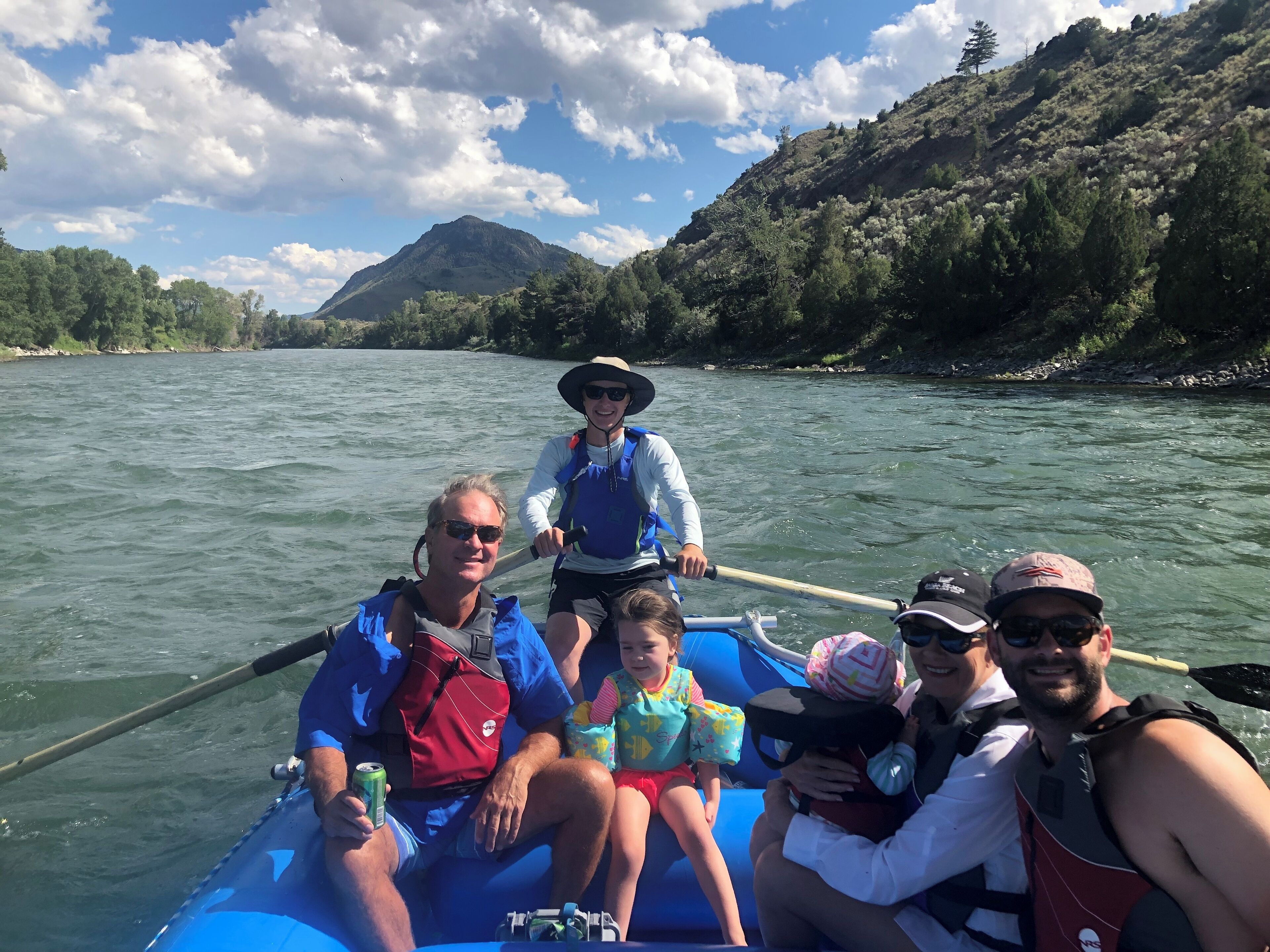 A group of people on a riverboat, with a mountainous landscape in the background.