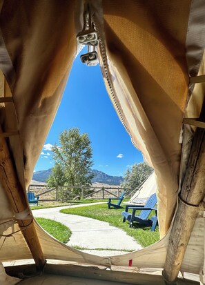 A view through a fabric structure with a clear sky, a grassy area, and a mountain in the background. - Yellowstone Tipis (Gardiner)