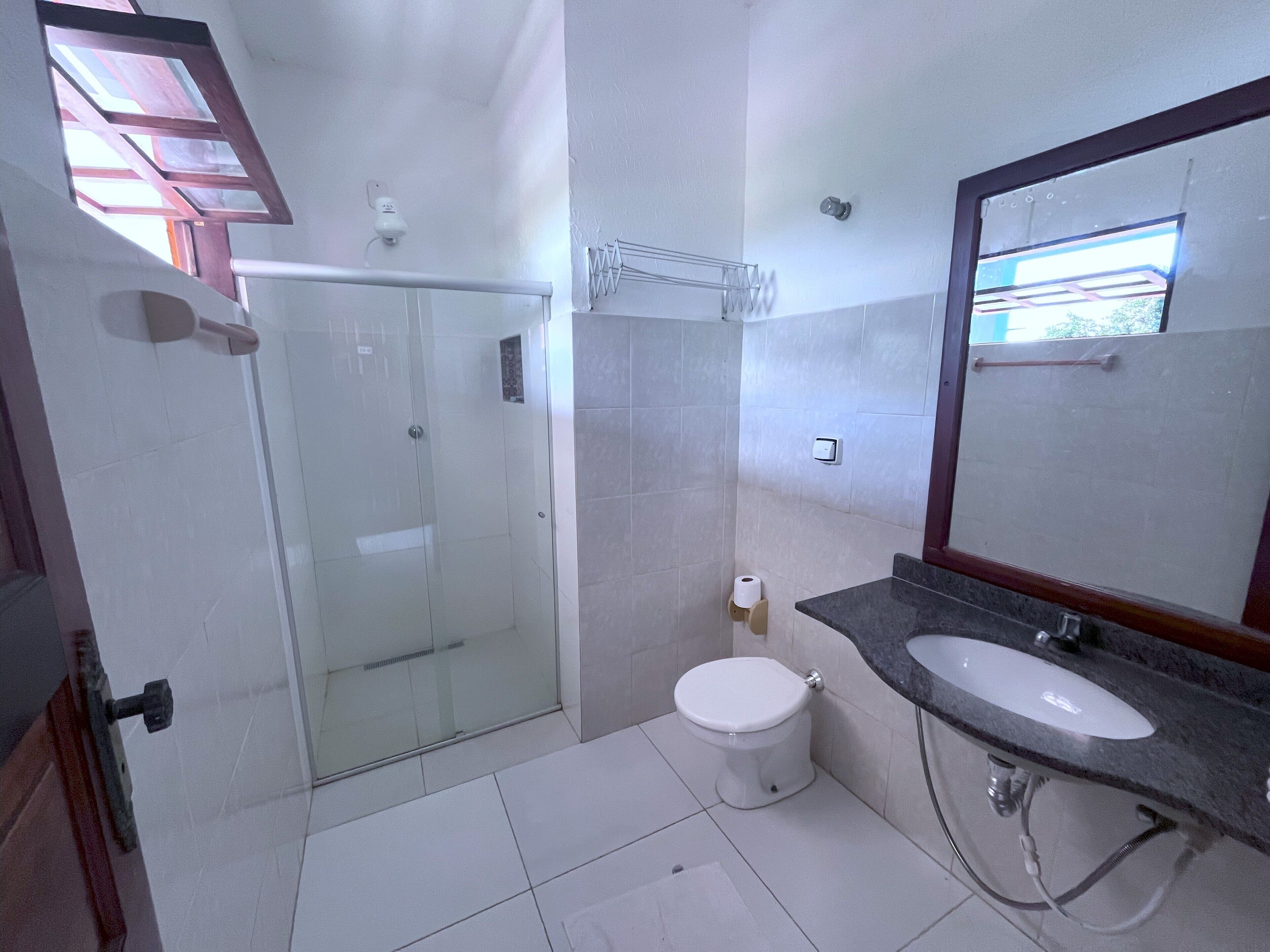 Ein Badezimmer mit Duschkabine aus Glas, Toilette, Waschbecken mit Spiegel und Handtuchhalter.