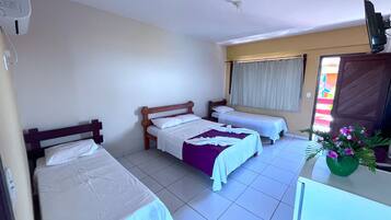 A hotel room with three single beds, a small desk, a television, and a window with curtains.