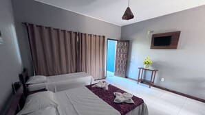 Habitación de hotel con dos camas, un televisor montado en la pared, una mesita con un jarrón de flores y una puerta que da a un balcón.