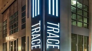 Un bâtiment dont la façade est ornée de deux panneaux lumineux verticaux sur lesquels on peut lire le mot « TRACE ».