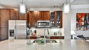 A modern kitchen with wooden cabinets, stainless steel appliances, and pendant lighting. - Commuter-friendly 1BR| nr MARTA Stations | Midtown (Atlanta)