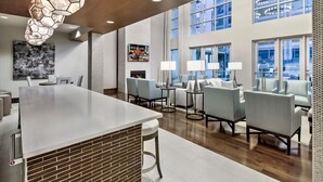 A modern hotel lobby with a large bar area, seating with tables, and large windows offering views.