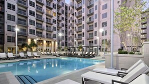 A modern hotel with a pool area, lounge chairs, and a multi-story building with balconies.