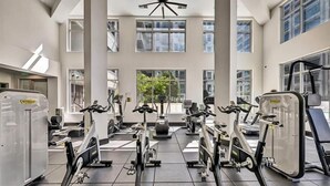 A gym with multiple cardio machines, large windows, and a modern ceiling design.