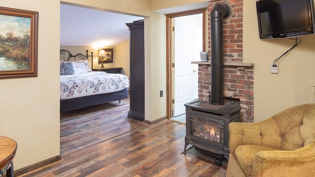 A cozy room with a wooden floor, a bed with floral bedding, a fireplace, and a television mounted on the wall. - Perfect Moment Cottage (Blowing Rock)