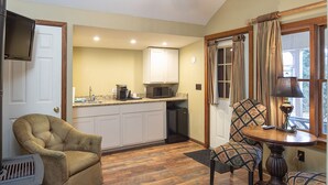 A compact kitchen with white cabinets, a microwave, and a coffee maker. There is a dining area with a table and two chairs, one with a patterned cushion. A fireplace is visible on the left side. - Perfect Moment Cottage (Blowing Rock)