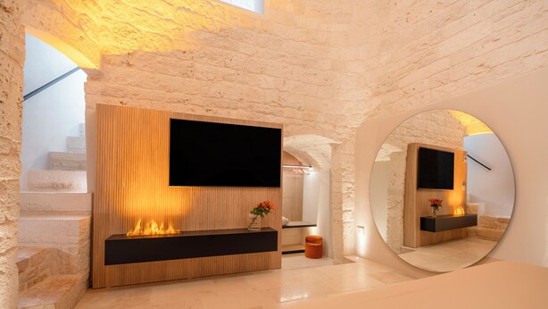 A modern bedroom with a fireplace, a TV mounted on a wooden wall, and a large mirror.