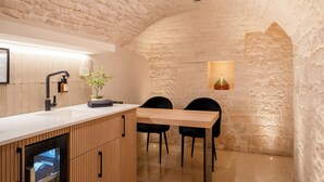 A modern kitchen with a stone wall, wooden cabinetry, a sink, and two black chairs.