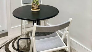 Une table de salle à manger ronde, avec un plateau en verre et une seule chaise dotée d’un siège et d’un dossier rembourrés de couleur grise.
